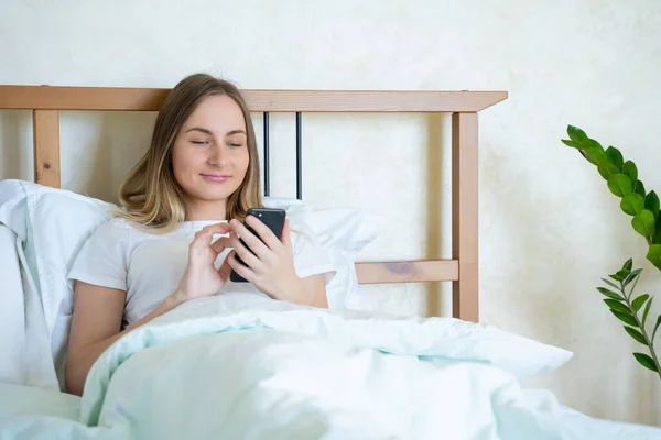 Mujer en la cama revisando aplicaciones sociales con smartphone — Foto de Stock