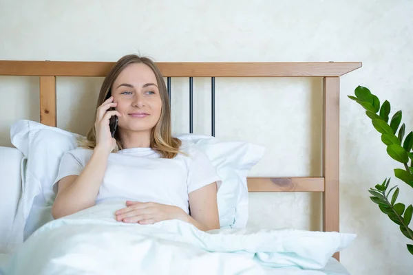 Mujer acostada en la cama, hablando por teléfono móvil y sonriendo — Foto de Stock