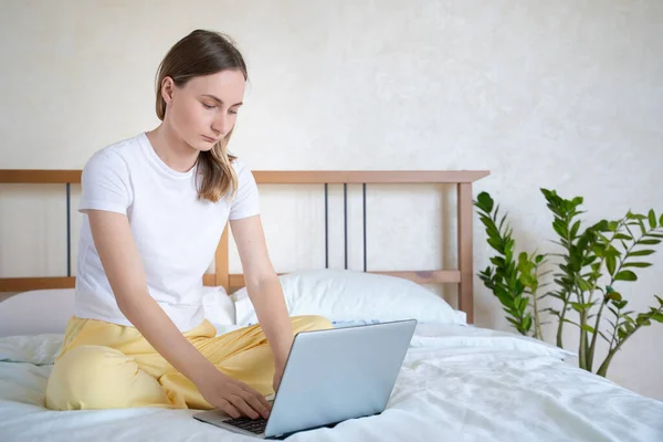 Mujer trabajando en una laptop sentada en la cama de la casa . — Foto de Stock