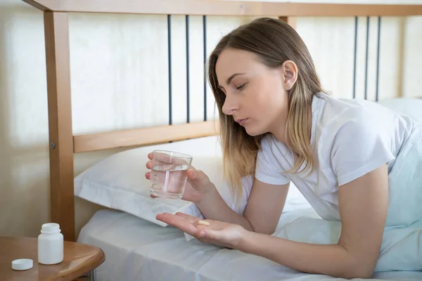 Jovem toma pílulas para dormir e vai dormir na cama — Fotografia de Stock