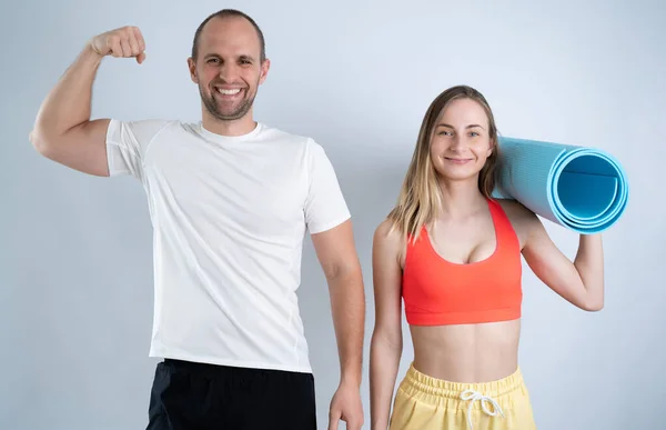 Счастливая спортивная пара держит фитнес мат и мужчина показывает бицепсы — стоковое фото