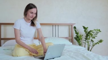 Dizüstü bilgisayar kullanan, yatakta oturan, başarıyı kutlayan, online piyango kazanan, iyi mesajlar okuyan, yatak odasında sosyal ağda sohbet eden bir kadın.