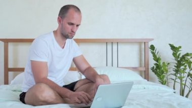 Mutlu adam başarıyı kutluyor, el kol hareketi yapıyor, bağırıyor, laptopla yatak odasında çalışıyor.