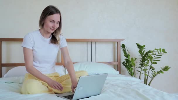 女性はラップトップを使用して、ベッドに座って、成功を祝い、オンライン宝くじの勝利を祝い、良いメッセージを読み、自宅で寝室のソーシャルネットワークでチャット — ストック動画