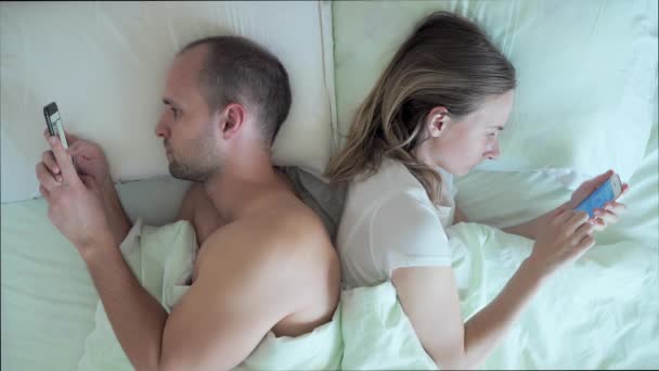 Paar liegt mit Handy im Bett und ignoriert sich gegenseitig. Mann und Frau süchtig nach Smartphone-Technologie in sozialen Netzwerken. — Stockvideo