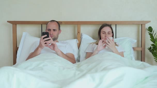 Ett par liggandes i sängen med mobiltelefon medan de ignorerar varandra. Man och kvinna beroende av smartphone sociala nätverk teknik. — Stockvideo