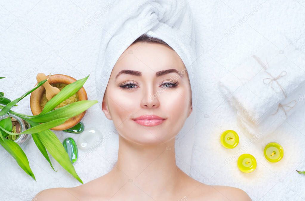 Spa girl with towel on head applying facial clay mask