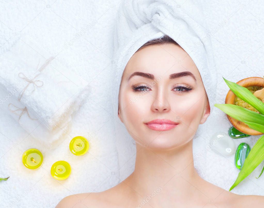 Spa girl with towel on head applying facial clay mask