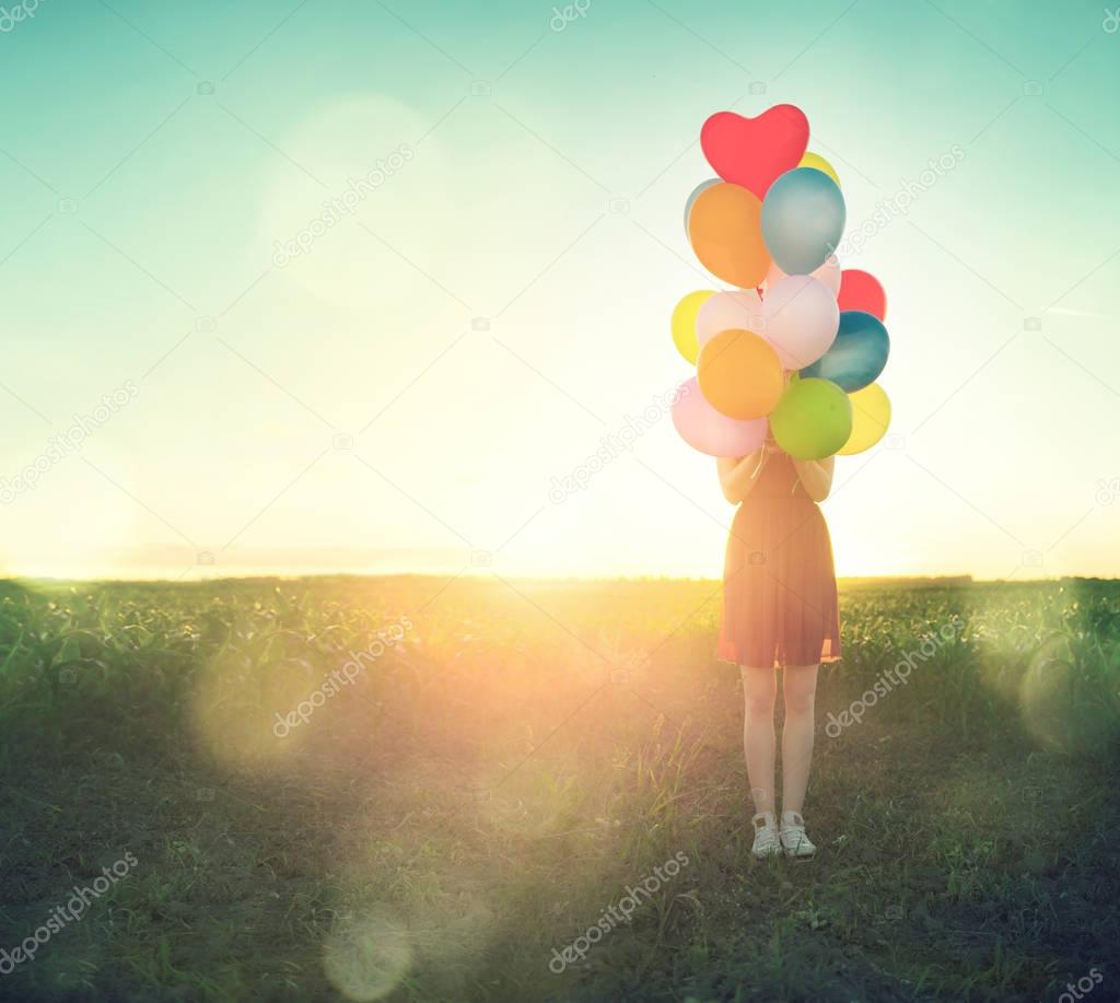 teenage girl on summer field with colorful air balloons over clear sky