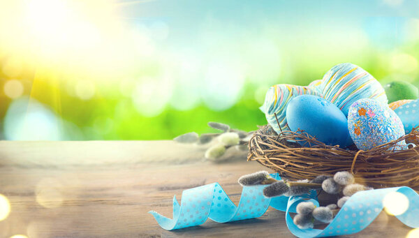 Пасхальные красочные окрашенные яйца с весенними цветами и синей атласной лентой на деревянном столе
 