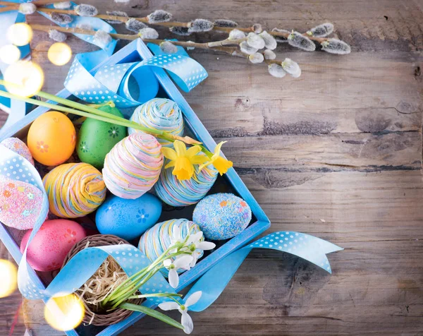 复活节五颜六色的彩蛋与春天的花朵和蓝色缎带在木桌上 — 图库照片