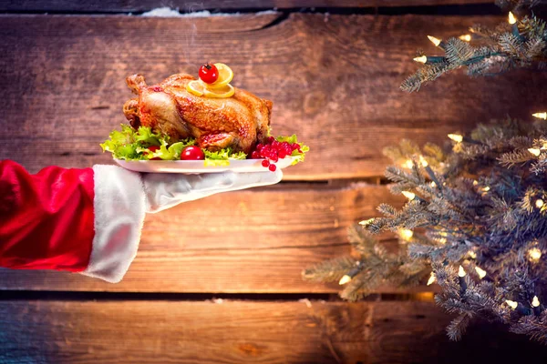 Christmas holiday dinner. Santa's hand holding roasted chicken o — Stock Photo, Image