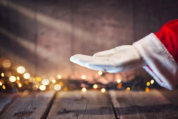 Weihnachtsmann Zeigt Geöffnete Handpalme Auf Holzgrund Mit Girlanden lizenzfreie Stockbilder