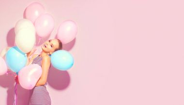 Eğleniyor pembe arka plan üzerinde renkli hava balonları ile neşeli genç kız