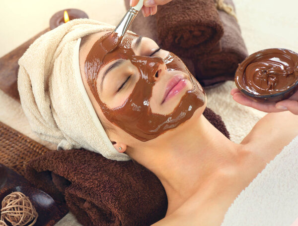 young woman relaxing in spa salon, applying chocolate face mask