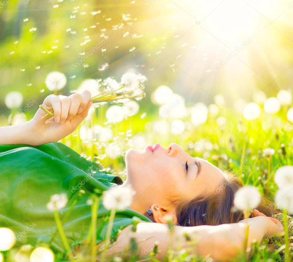 Young woman lying on field in grass and blowing on dandelions