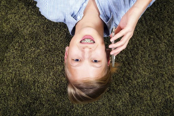Adolescent avec téléphone.Avoir du plaisir adolescent se trouve sur un tapis . — Photo