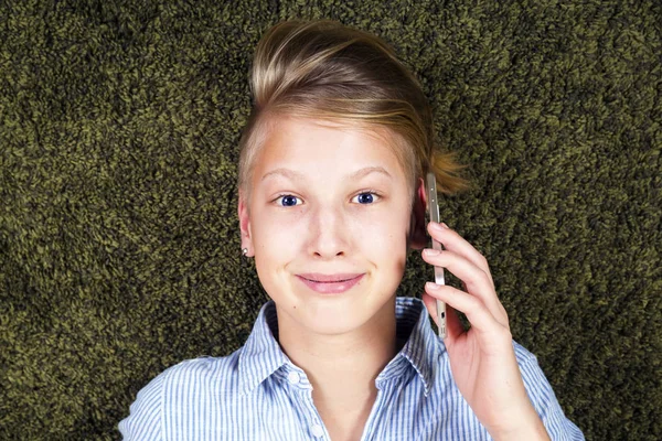 Adolescente con teléfono. Divertirse adolescente se encuentra en una alfombra . — Foto de Stock
