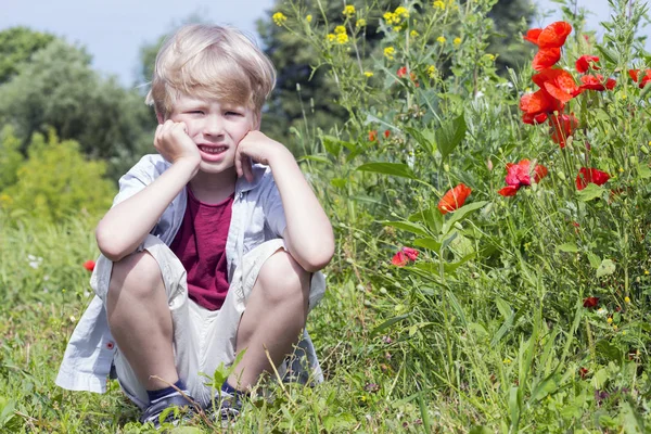 Bom menino loiro senta-se no campo, primavera — Fotografia de Stock