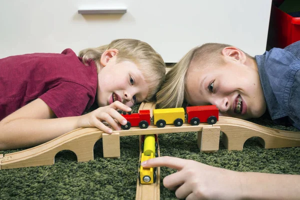 Hermanos juegan con tren de madera, construir ferrocarril de juguete en casa o d —  Fotos de Stock