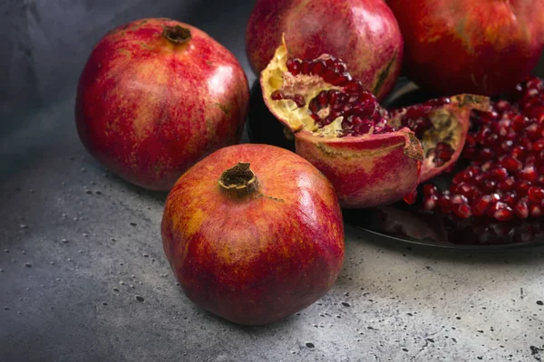 Red juice pomegranate on black plate on gray concrete background.