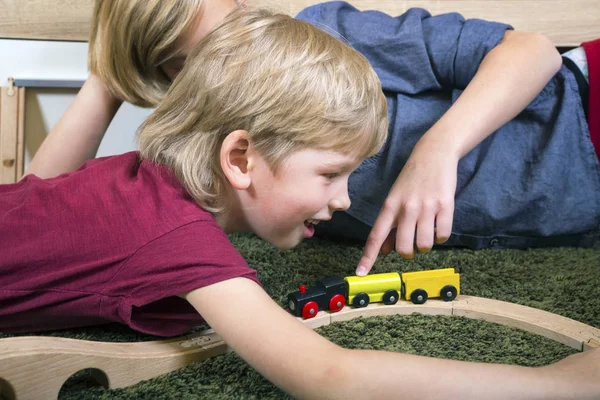 Hermanos juegan con tren de madera, construir ferrocarril de juguete en casa o d —  Fotos de Stock