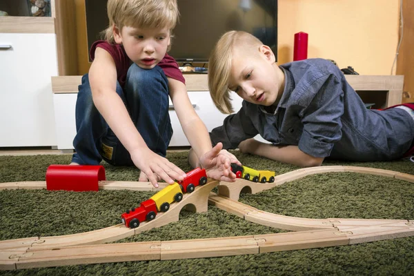 I fratelli giocano con il treno di legno, costruiscono ferrovie giocattolo a casa o d — Foto Stock