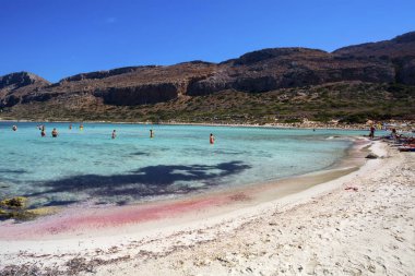 Yunanistan 'ın Girit adasındaki Balos gölü. Pembe kum. Turistler Balos sahilinin berrak sularında dinleniyor..