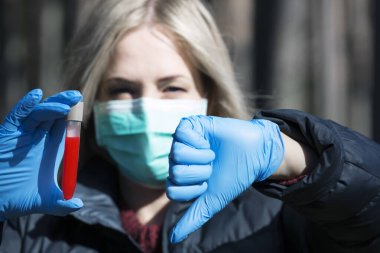 Yüzünde koruyucu steril tıbbi maske takan bir kadın, elinde kanla test tüpü tutuyor. Hava kirliliği, virüs, Çin salgını koronavirüs konsepti.
