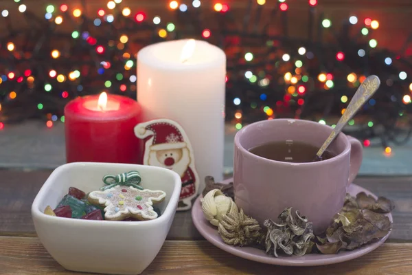 Festive still life with a cup of tea, bowl of candies and burning candles — Stock Photo, Image