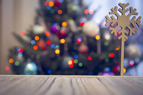 A wooden snowflake on a wooden table against decorated Christmas tree — Stock Photo, Image