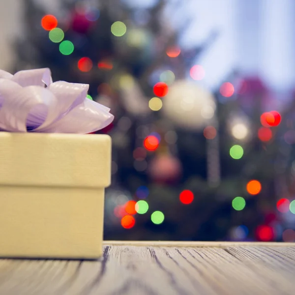 Gift box on a wooden table against decorated Christmas tree — Stock Photo, Image