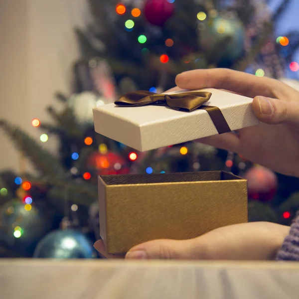 Χέρια κλείσιμο κουτί δώρου σε ένα ξύλινο τραπέζι ενάντια στολισμένο χριστουγεννιάτικο δέντρο — Φωτογραφία Αρχείου