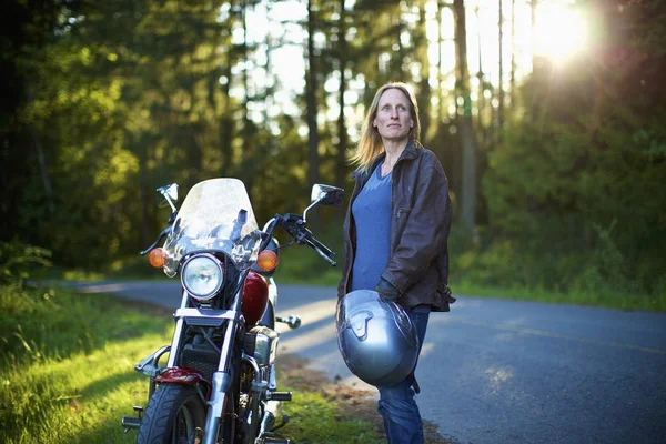 Confident woman standing at motorcycle at roadside in woods — Stock Photo