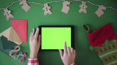 Yeşil arka plan kavramı üzerinde Noel dekorasyonu. Kadın el ile yeşil ekran tablet cihaz kullanarak. Tablo üstten görünüm. Chroma anahtar. Çalmak, dokunarak