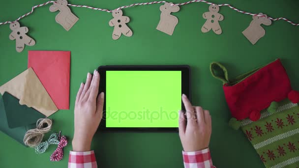 Вид зверху таблиці. Жінка збільшує зображення, знімаючи на планшеті зелений екран. Ключ хроми. Новорічна концепція — стокове відео