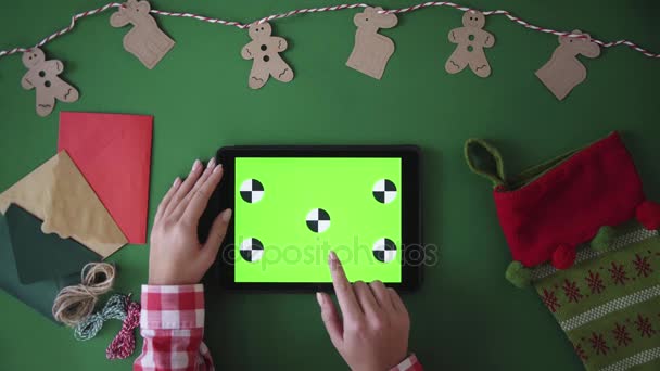 Weihnachtstischplatte von oben betrachtet. Der weibliche Finger macht verschiedene Gesten auf dem Tablet mit grünem Bildschirm. Chroma-Schlüssel. Tracking-Bewegung. — Stockvideo