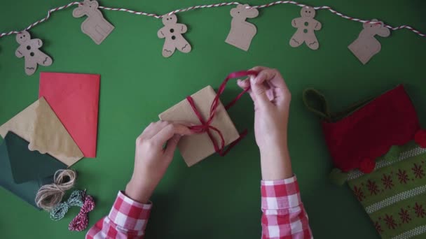 크리스마스에 크리스마스 훈장을 가진 녹색 테이블 배경 선물에 리본을 만들려고 노력 하는 여자. 위에서 상위 뷰. — 비디오