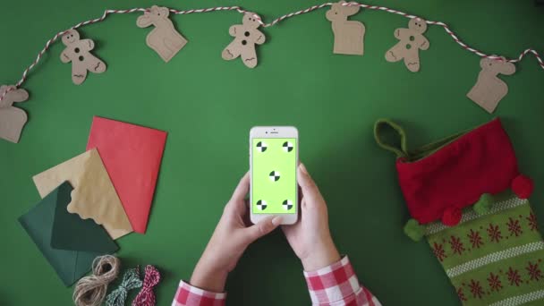 Mujer desplazándose hacia arriba en el teléfono inteligente con pantalla verde. Mesa de Navidad concepto de vista superior. Clave de croma. Movimiento de seguimiento — Vídeos de Stock