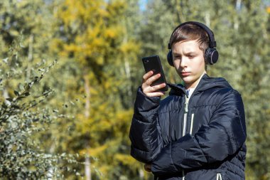 Adam kulaklıklar müzik dinler ve ağaçlar arka planı güneşli bir sonbahar gününde onun telefona benziyor.