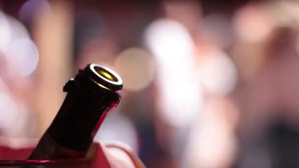 Live opnamen van de hals van een fles champagne tegen de achtergrond van de knipperende lichten op een feestje. — Stockvideo
