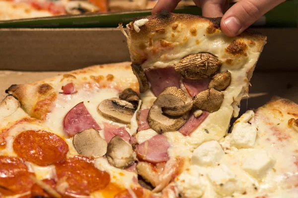 Personens hand tar den första bit av pizza med svamp. — Stockfoto