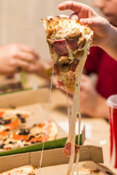 Рука подростка держит кусочек пиццы, из которой вытягивается расплавленный сыр. . — стоковое фото