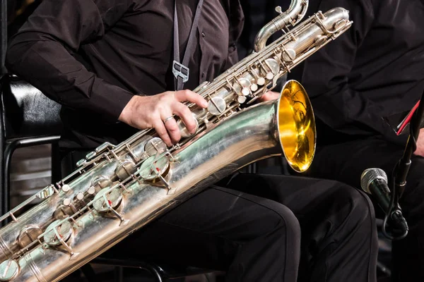 El saxofonista del colectivo de jazz se sienta en una silla y se pone un saxofón barítono de rodillas . — Foto de Stock