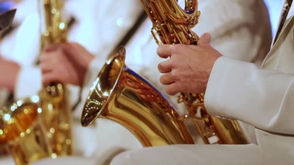 A mão de um homem num fato branco num saxofone dourado numa banda de jazz. Close-up. Profundidade de campo rasa . — Vídeo de Stock