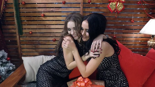 Schöne brünette und blonde Mädchen in schwarzen Abendkleidern umarmen sich nach dem Austausch von Neujahrsgeschenken. — Stockfoto