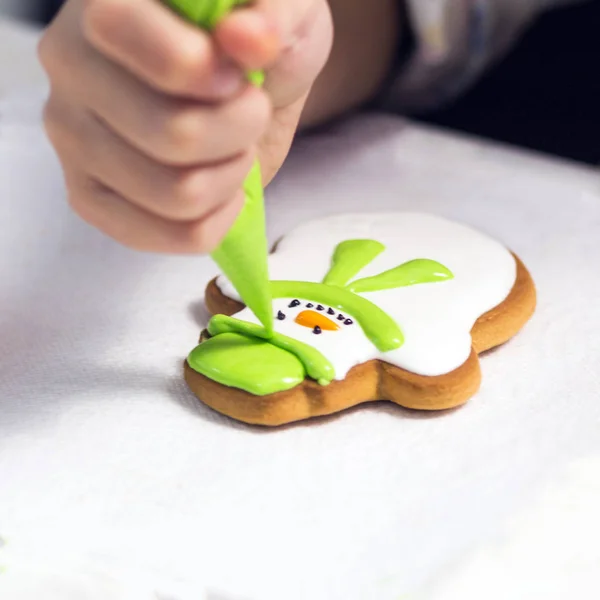 Пеку праздничное печенье. Детские руки украшают пряники в виде снеговика с сахарной глазурью с помощью пакетика. Рождественские угощения . — стоковое фото