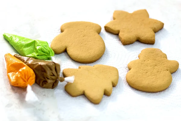 Four Christmas gingerbread and piping bags with a glaze of green, brown and orange. Handmade cookies in the form of a mitten, a Christmas tree, a snowman and a snowflake. — Stock Photo, Image