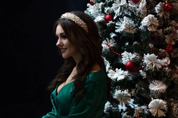 Schöne Mädchen in einem grünen Kleid in der Nähe des Neujahrsbaums auf schwarzem Hintergrund. — Stockfoto