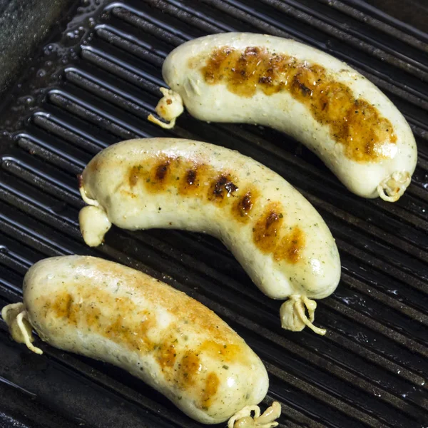 Grilled sausages for grilling in a black frying pan. Close-up. A square picture. — Stock Photo, Image